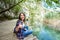 Portrait of young smiling tourist woman sitting on wooden bridge, showing thumbs up