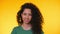 Portrait of young spanish student girl with curls on yellow background. Trendy cute woman smiling to camera. Studio