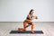 Portrait of young sporty healthy attractive woman in black top and orange leggings doing lunge with elastic latex resistance band