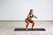 Portrait of young sporty healthy beautiful woman in black top and orange leggings doing squatting with elastic resistance band