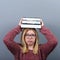 Portrait of a young student woman holding books on head against gray background.Tired of learning/studying concept