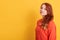 Portrait of young stunning model with red wavy hair, pretty woman in fashionable orange sweater, posing against yellow background