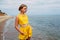 A portrait of a young tanned girl in yellow summer clothes stands on the seashore
