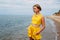 A portrait of a young tanned girl in yellow summer clothes stands on the seashore