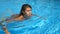 Portrait of young tanned woman refreshing and swimming in empty pool. Brunette girl floating at the basin of hotel and