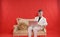 Portrait of a young teen man wearing white office suit and sitting on the golden luxury sofa on red background. he works on the la