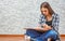 Portrait of young teenager brunette girl with long hair sitting on floor and drawing picture on gray wall background