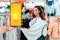 Portrait of a young thoughtful caucasian woman choosing clothes in a store. On the left side is a hand with a smartphone. The