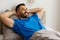 Portrait of a young well-slept man lying in bed, smiling to the side, enjoying the start of the day