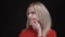 Portrait of young white-haired caucasian girl in red sweater looking at watches and feeling bored of waiting on black