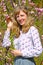 Portrait of the young woman against the background of the blossoming bushes of almonds three-blade