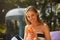 Portrait of young woman with cocktail glass near swimming pool on a deck chair with palm trees behind. Vacation concept