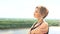 Portrait of young woman in countryside summer during windy day with river, trees, forest in background