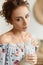 Portrait of young woman with curly hair and green eyes in the interior. Model girl posing with vase. Summertime