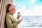 Portrait of a young woman with dreadlocks drinking coffee and using a smartphone. Sky and ocean on the background. The