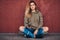 Portrait of a young woman dressed in a hoodie and ripped jeans leaning on a wall while sitting on a skateboard at a