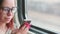 Portrait of young woman in glasses browsing mobile phone, riding on train. Close up. Pretty female using gadget while