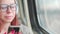 Portrait of young woman in glasses browsing mobile phone, riding on train. Close up. Pretty female using gadget while