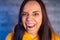 Portrait of young woman with grimacing face. Close up of crazy female in yellow hoodie monkeying on gray brick