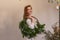 Portrait of young woman holding asymmetrical green Christmas wreath made of natural materials