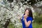 Portrait of a young woman holding a brunch of blossoming plum tree in garden, happily smiling, smelling the flowers, looking at th