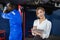 Portrait of young woman holding clipboard standing at workplace with mechanic in garage background. Female employees taking notes