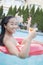 Portrait of young woman holding a drink and sitting on an inflatable tube in the pool