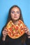 Portrait of young woman holding and eating pizza. Creative idea concept, funny mugshot with pizza