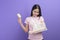 Portrait of young woman with an injured arm in a sling holding a credit card or medical insurance card over purple background in