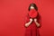 Portrait of young woman in lace dress hiding, covering face with cap, looking aside isolated on bright red wall