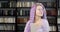 Portrait of a young woman with long colored purple hair and nose piercing standing in the library with a book. Smiling