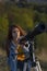 Portrait of young woman looking through the telescope on the hil