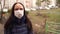 Portrait of young woman in medical mask on her face in yard on street. Adult female covered her face with mask to