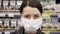 Portrait of young woman in medical mask stands in supermarket. Protection from coronavirus, purchase of food for quarantine.