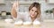 Portrait of young woman pastry chef pouring coconut flakes over cooked cakes. In the background is a white kitchen.