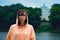 Portrait of young woman posing near lake in summertime. Female tourist standing and looking at camera on blurred