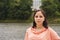 Portrait of young woman posing near lake in summertime. Female tourist standing and looking at camera on blurred