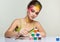 Portrait of young woman posing at the table with pyramid of small cans of paint and brush in hand