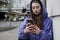 Portrait of a young woman in a purple hooded sweat using her smartphone