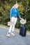 Portrait of young woman putting floppy hat on handle of black suitcase, holding cardboard with inscription anywhere.