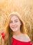 Portrait of a young woman in red dress on a background of golden oats field, summer outdoors