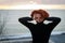 Portrait of a young woman with red hair and piercing look on the background of the sea and sunset