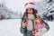 Portrait of young woman in Santa hat using phone on smartphone in snowy winter park holding heap of Christmas presents