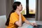 Portrait of a young woman sitting at a desk with headphones on, using a laptop. A window in the background. The concept of online