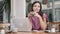 Portrait of young woman sitting with laptop and drinks coffee in cafe