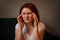 Portrait of a young woman sitting on a sofa with closed eyes and fingers pressed to her temples. Health issues, migraine, headache