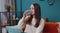 Portrait of young woman sitting on sofa at home holds glass drinks water, makes gulp of clean aqua