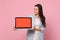 Portrait of young woman in striped jacket hold looking on laptop pc computer with blank empty screen isolated on pink