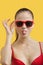 Portrait of young woman in sunglasses sticking out tongue over yellow background