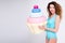 Portrait of young woman in swimsuit posing with giant cupcake over gray